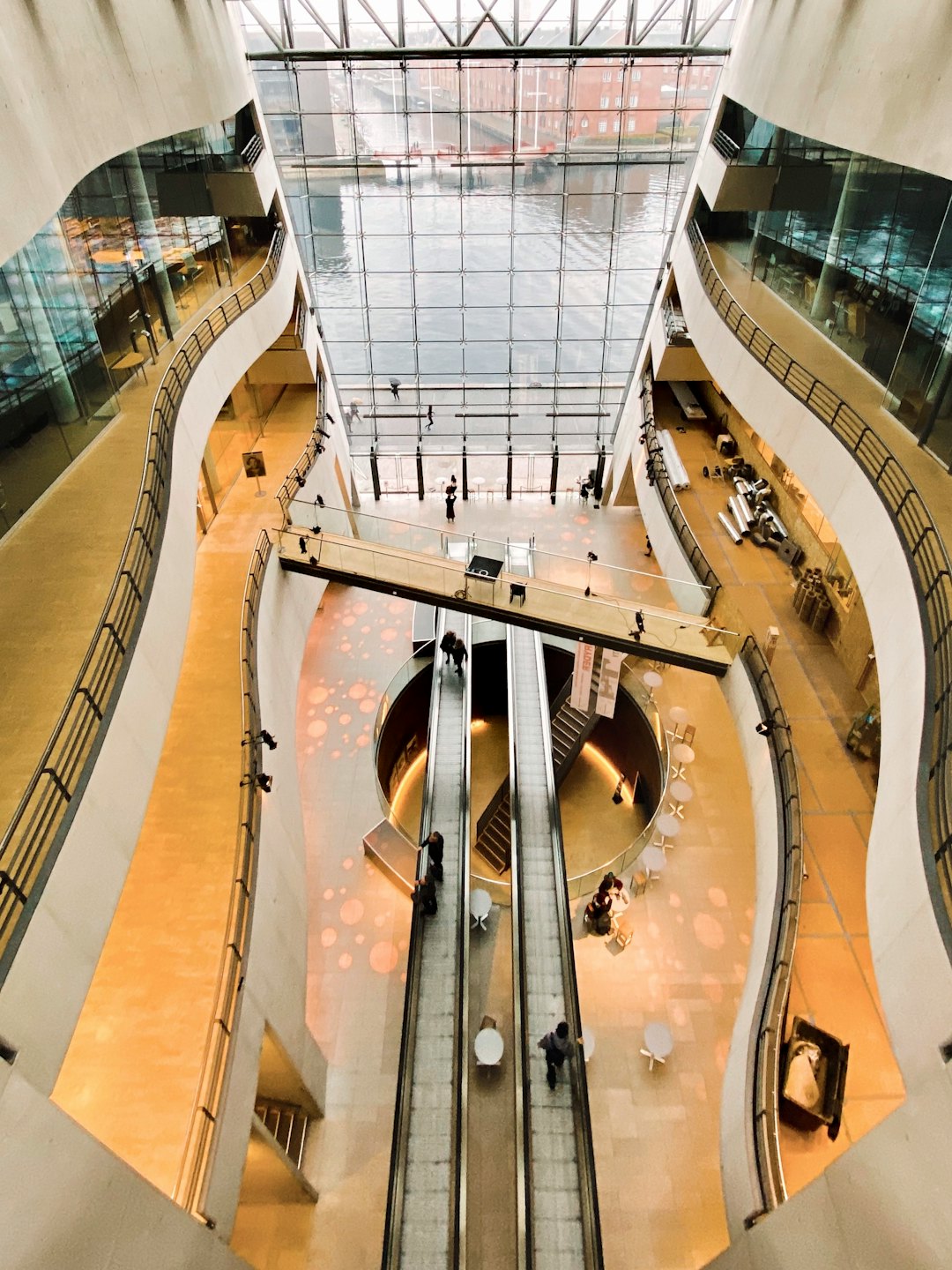 Nowoczesna architektura atrium z ludźmi na kładkach i ruchomych schodach.