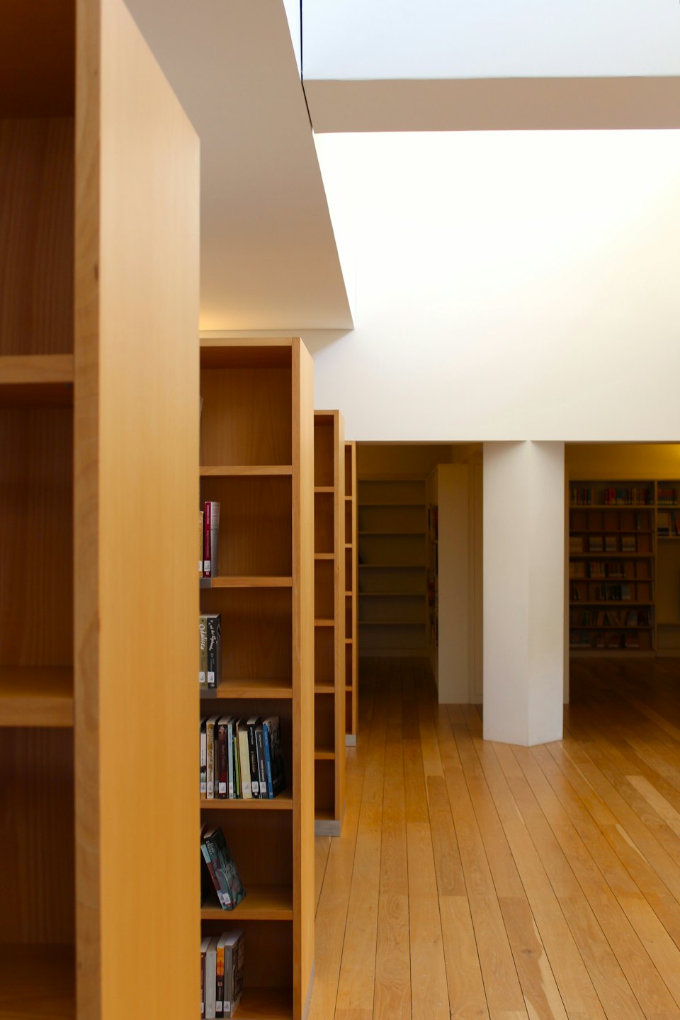 Nowoczesne wnętrze biblioteki z rzędami jasnych drewnianych regałów.