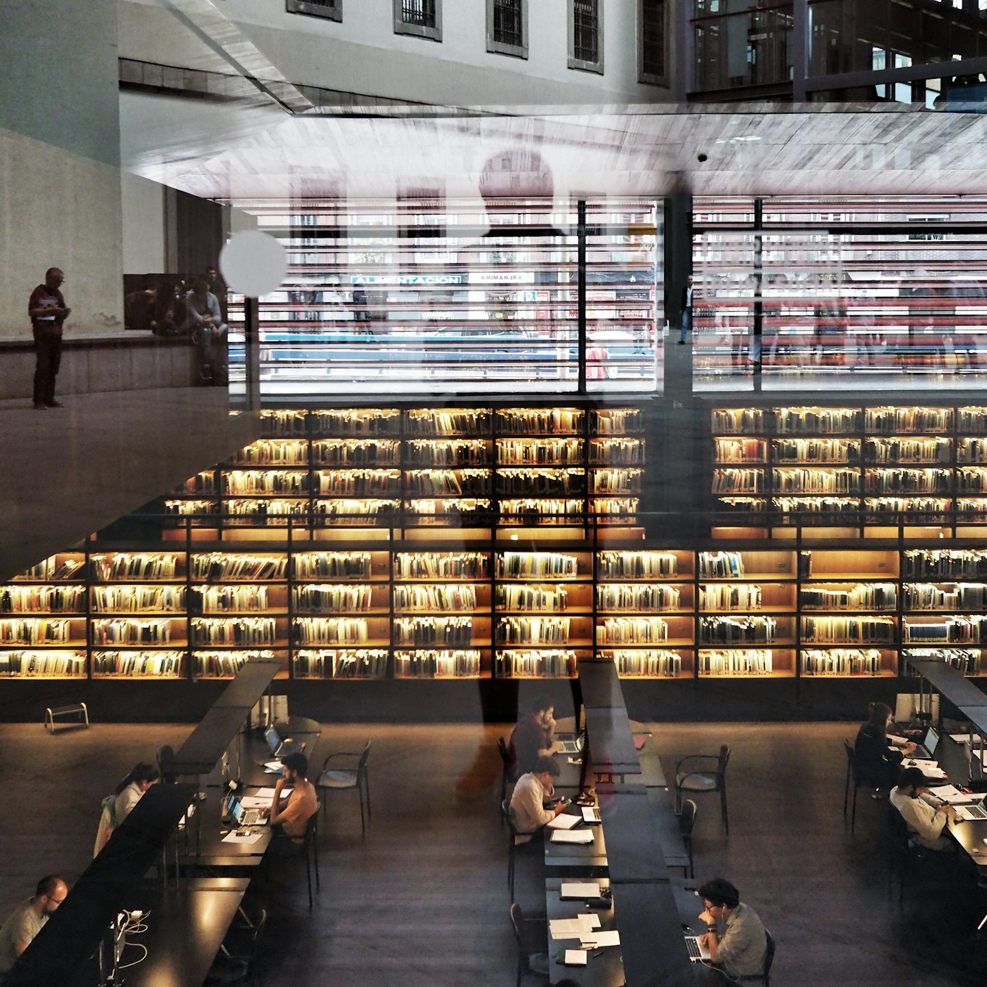 Ludzie uczący się i pracujący w nowoczesnej bibliotece z wieloma regałami.