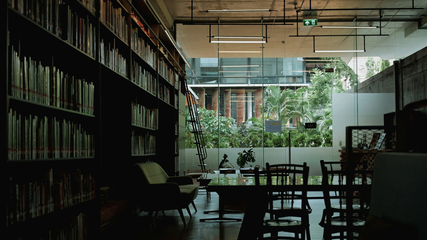 Nowoczesna czytelnia biblioteczna z regałami i stołami z widokiem na drzewa.
